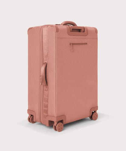3/4 back view of Sydney checked rolling luggage 28.5” in warm dust pink showing side handle and back zippered phone/passport pocket